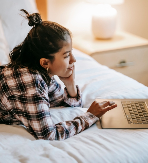 Jonge vrouw ligt op bed met laptop.