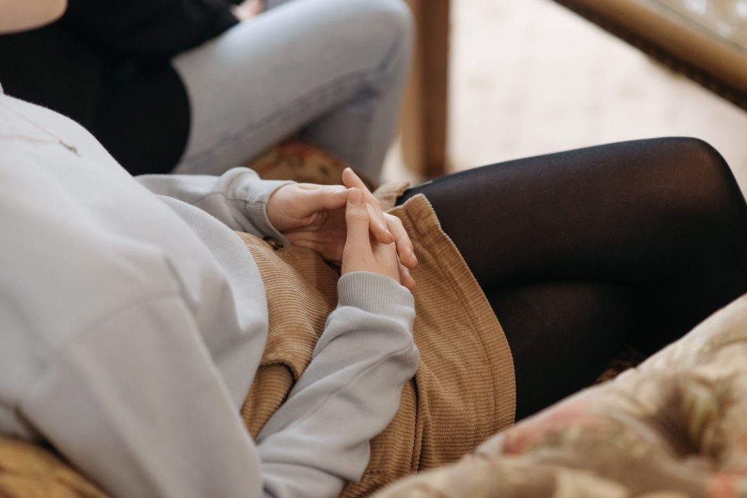 Persoon zit met gevouwen handen tijdens een gesprek met een hulpverlener.