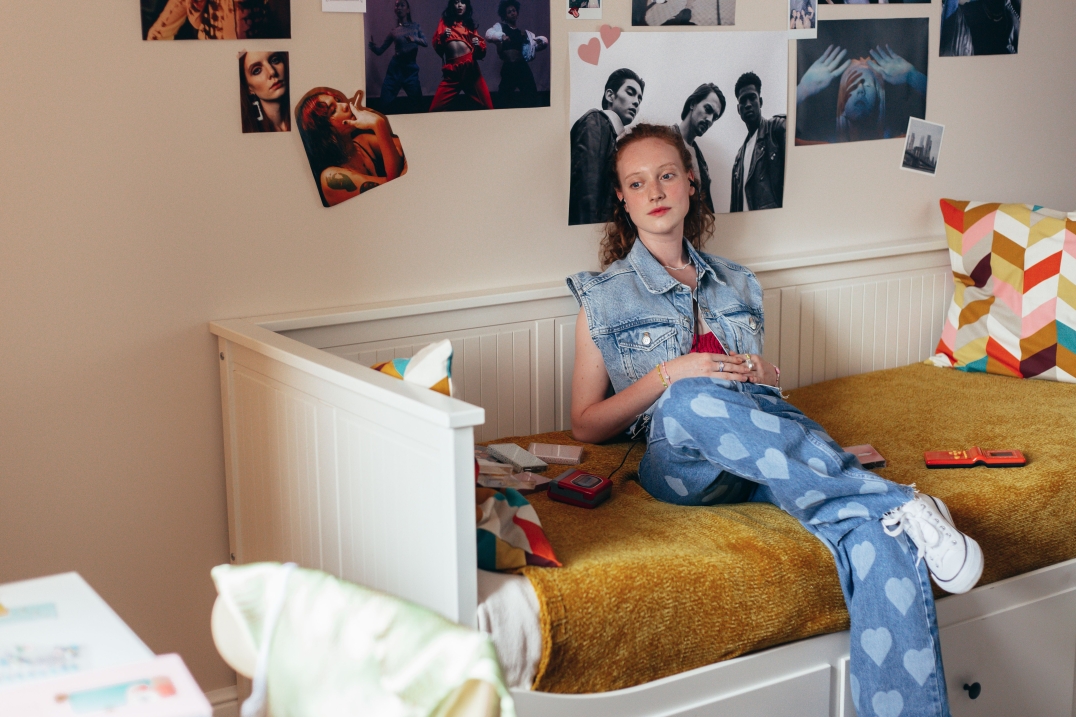 Jonge vrouw met krullend haar die op een bed naar muziek luistert.