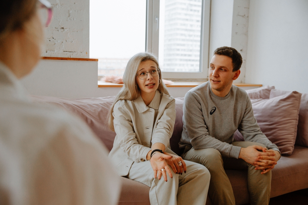 Twee mensen zitten op een bank tijdens een gesprek in een lichte kamer.