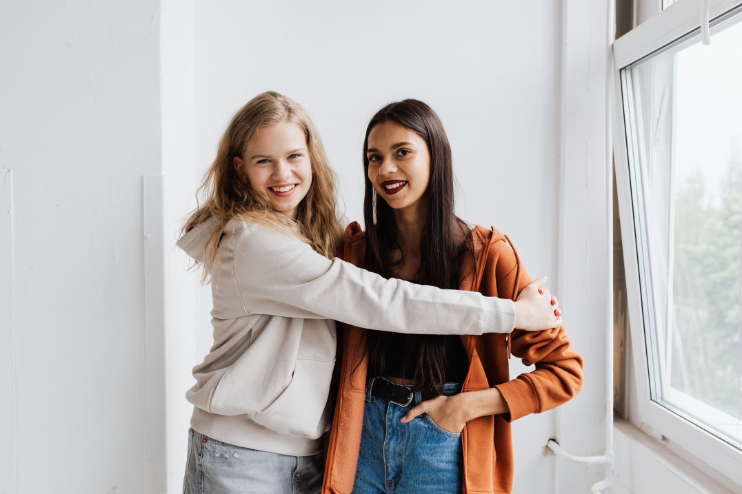 Twee jonge vrouwen omhelzen elkaar en lachen naar de camera.