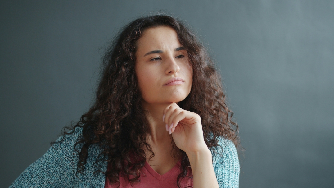 Vrouw kijkt nadenkend voor zich uit met hand onder haar kin.